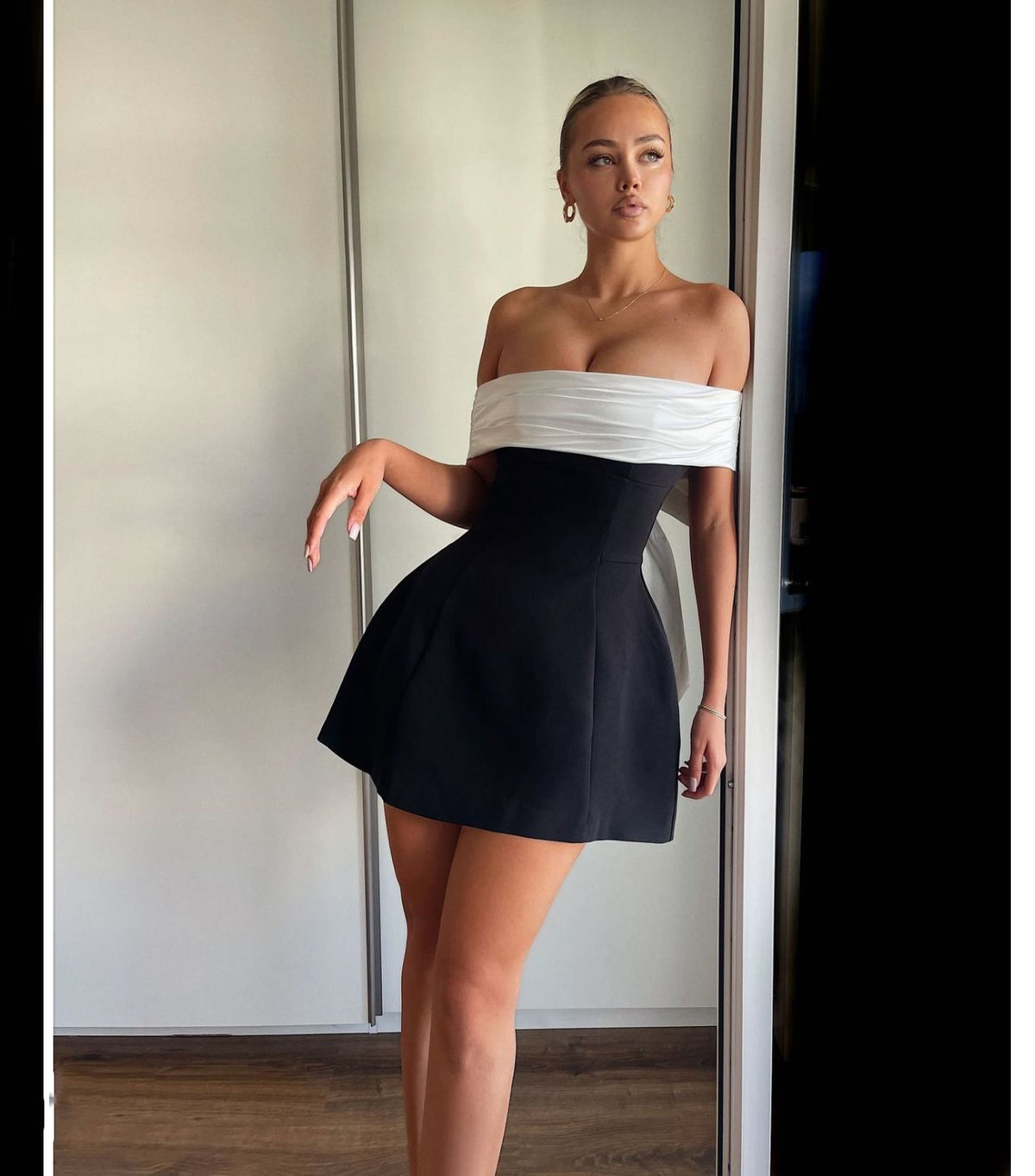 Vestido con hombros descubiertos, color blanco y negro en contraste, cintura ajustada, diseño swing y lazo